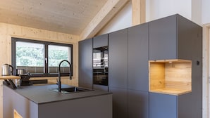Une cuisine moderne dotée d’un îlot central, d’appareils électroménagers intégrés et d’une fenêtre donnant sur la verdure.