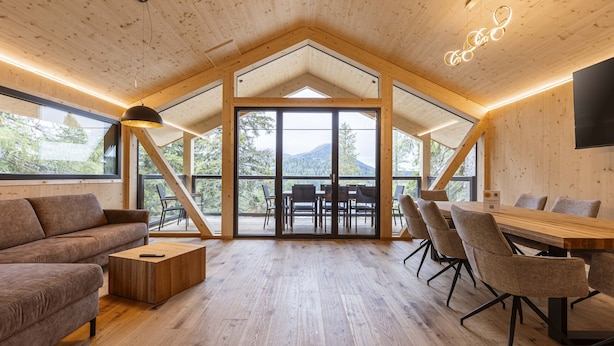 Une pièce spacieuse avec un plafond haut, des poutres apparentes, une grande table avec des chaises, un canapé et une table basse.