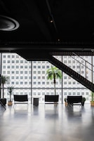 A modern interior with a staircase, large windows, and several seating areas.