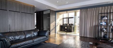 A modern living room with a leather sofa, a coffee table, and a glass door leading to a kitchen.