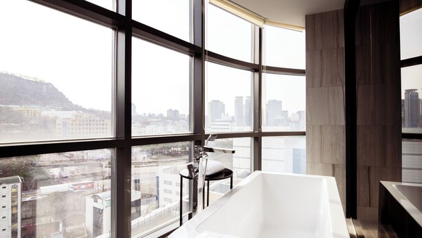 A modern bathroom with a large bathtub, a view of the city through floor-to-ceiling windows, and a minimalist design. - HOMESRED MYEONGDONG (Seoul)