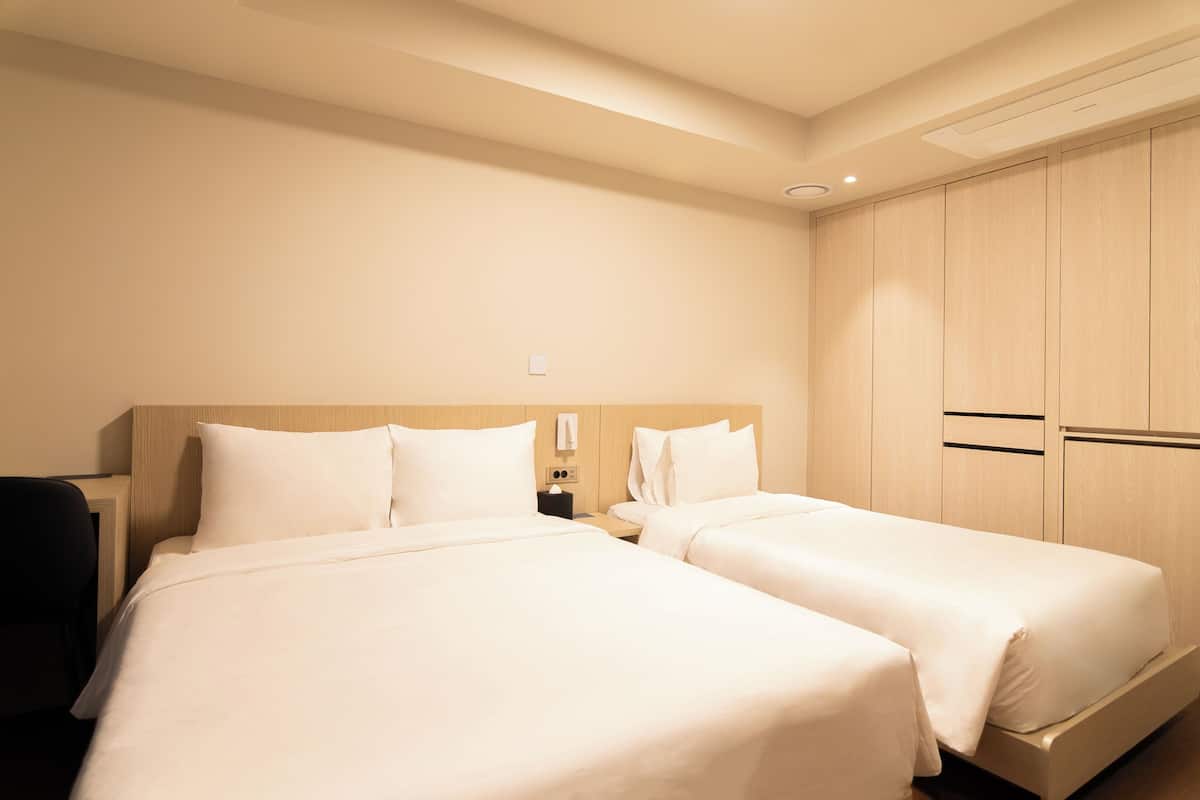 A hotel room with two beds, a wooden wardrobe, and a nightstand with a lamp.