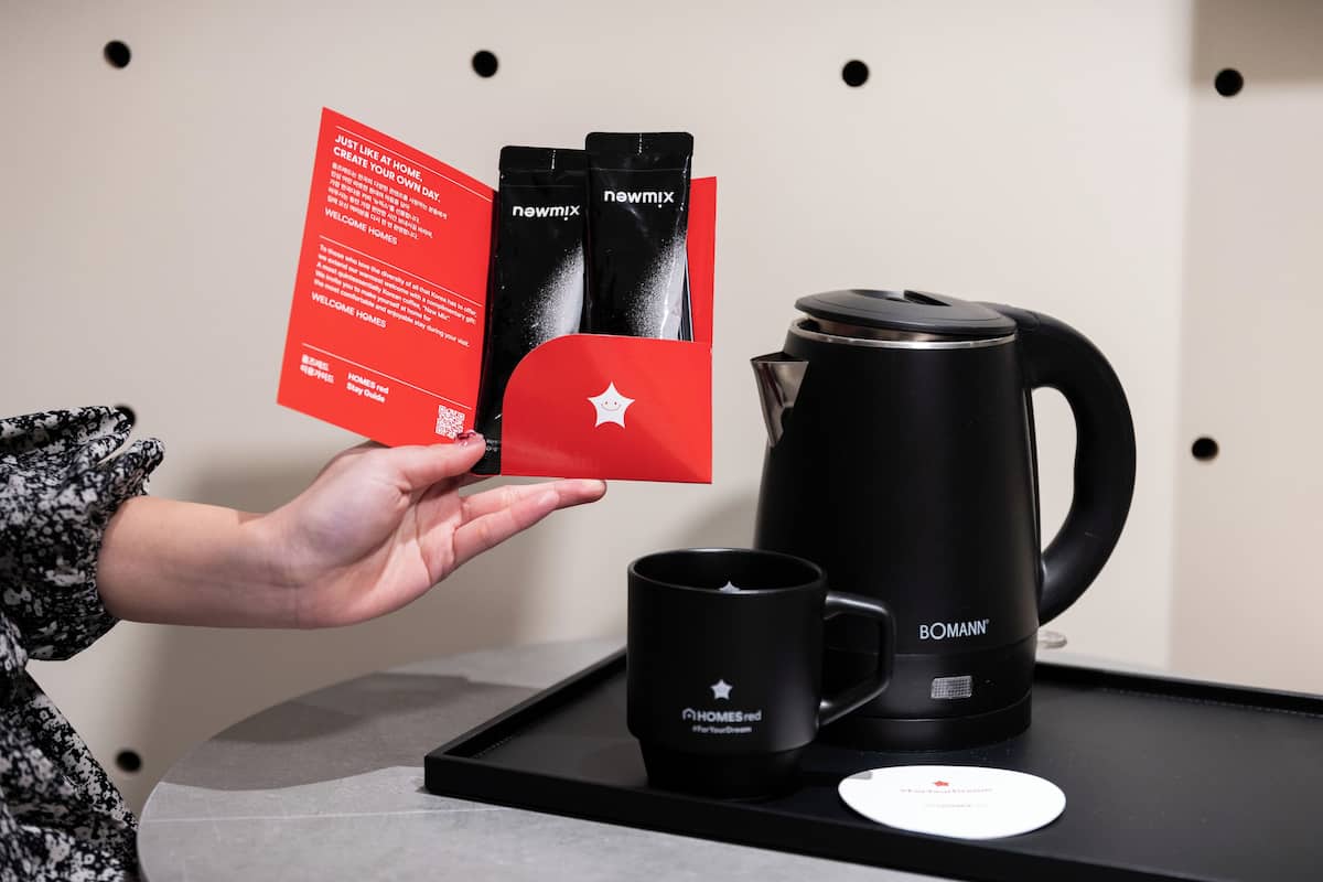 A person holding a red brochure with black coffee pods and a black coffee maker on a tray.