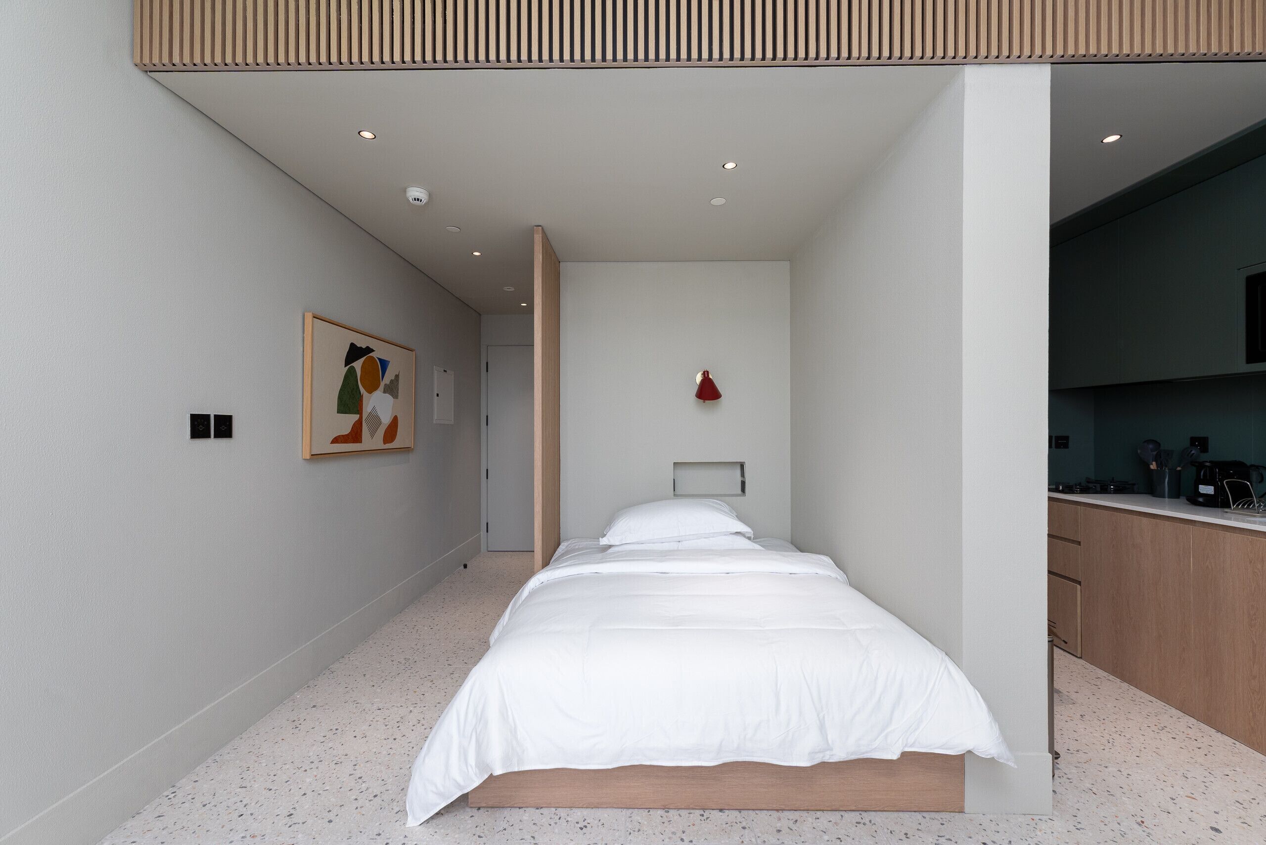 Une chambre à coucher moderne avec un grand lit, une petite table de chevet et un luminaire fixé au mur.
