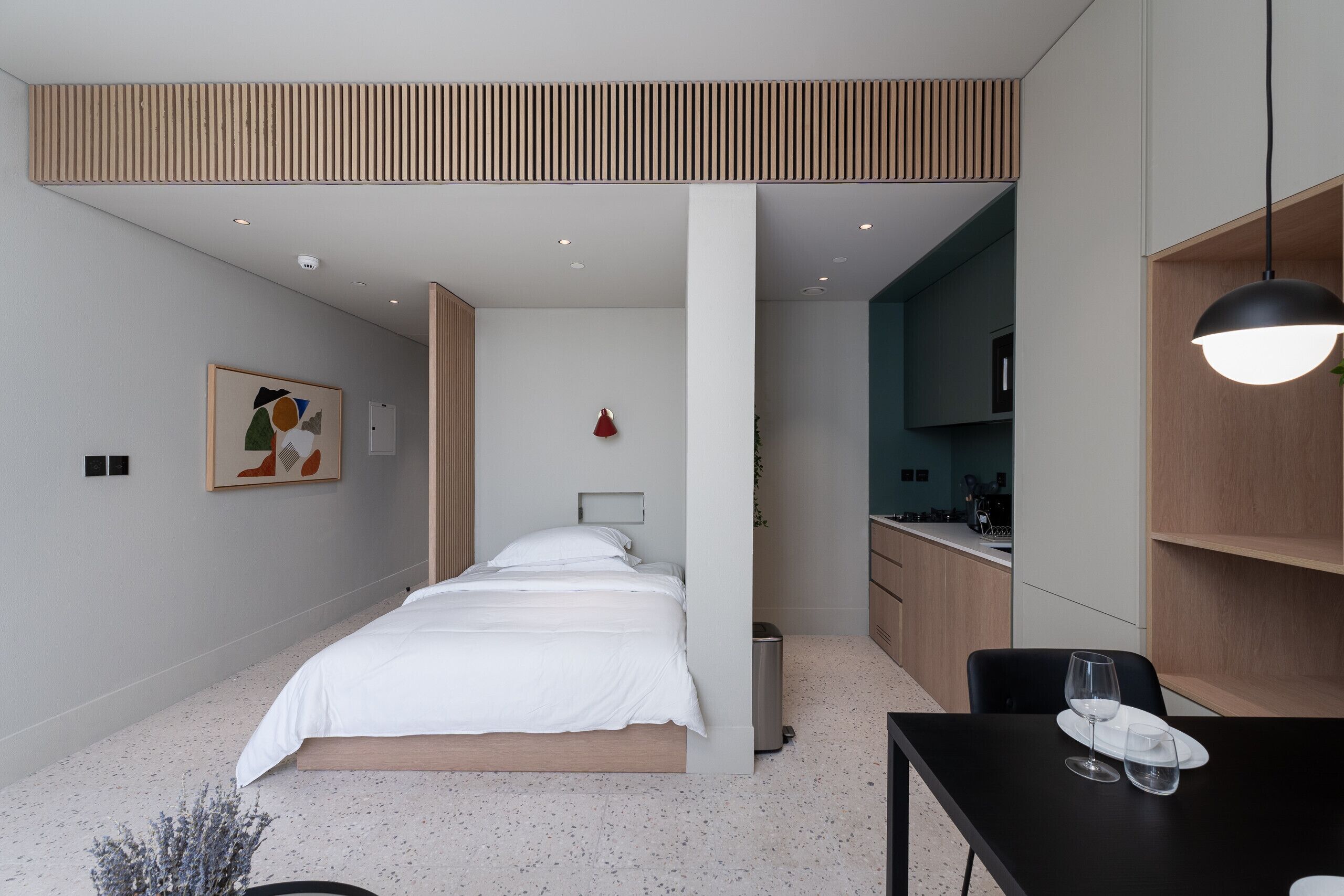 A modern hotel room with a bed, a desk, and a kitchenette.