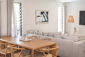 A living room with a wooden dining table, beige sofa, and a framed picture on the wall. - Coastal Calm - Oceanstays (Yamba)