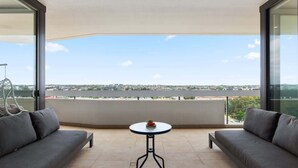 A balcony with two grey sofas, a small round table, and a clear view of a cityscape. - Luxe 2-Bed: Modern Interiors, Balcony & BBQ Area (Lidcombe)