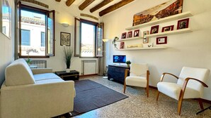 Una sala de estar con sofá, sillas, televisor y una pared decorada con cuadros.