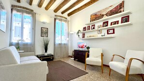 A living room with a sofa, armchairs, a small table, a TV, and a wall with framed pictures. - Residence Moretta (Historical Center) (Venecia)