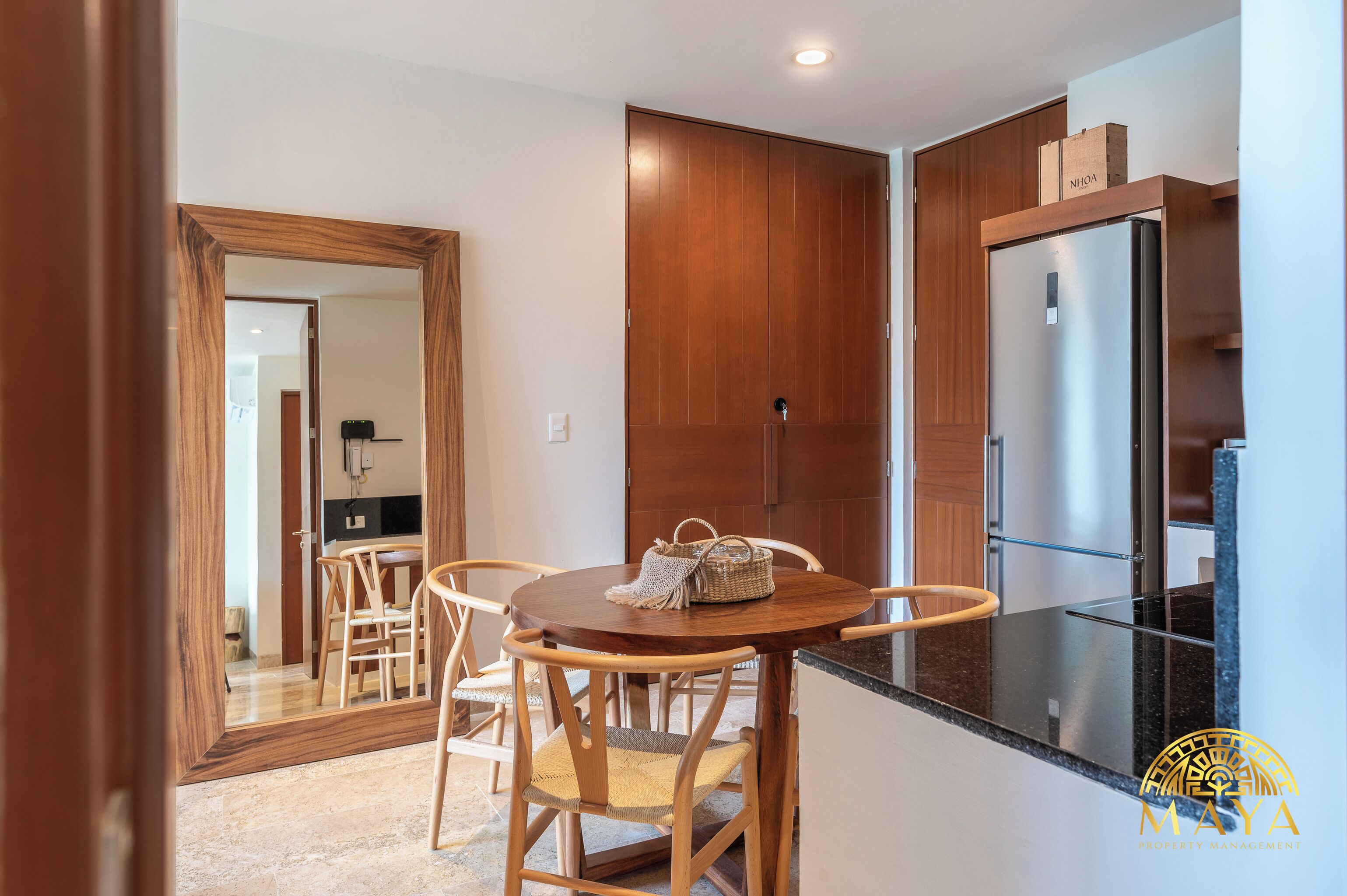 A modern kitchen with wooden cabinets, a stainless steel refrigerator, and a dining area with a round table and chairs.