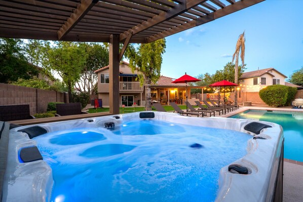 A hot tub area with a pool, lounge chairs, and a covered patio.