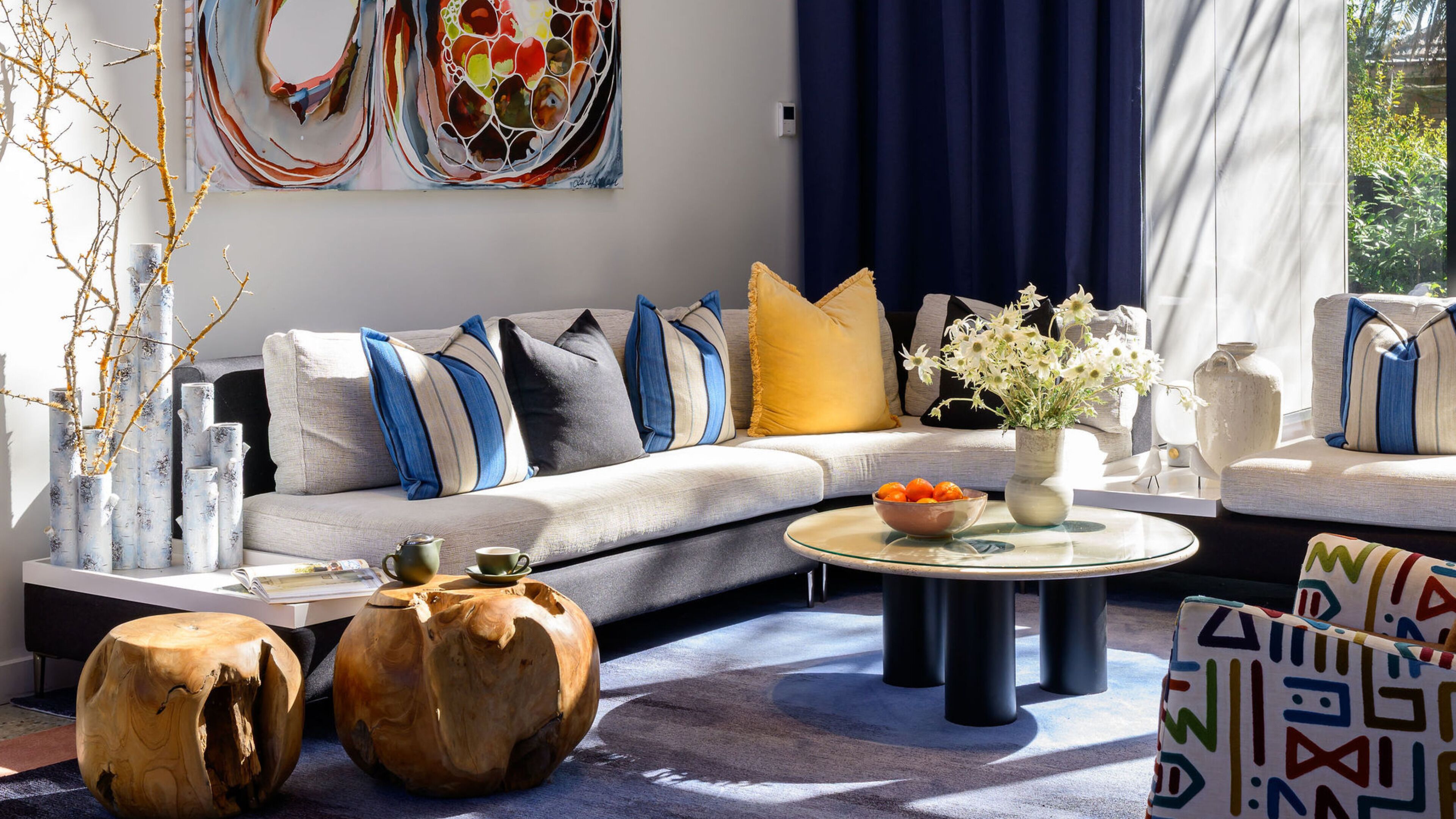 A modern living room with a grey sofa, blue and yellow cushions, a glass coffee table, and decorative vases.