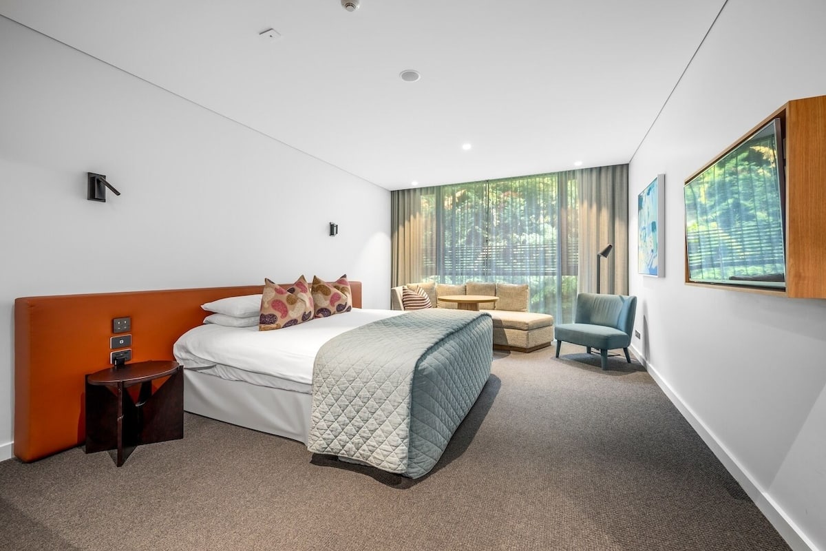 Una habitación de hotel moderna con cama, zona de estar y ventanas amplias.