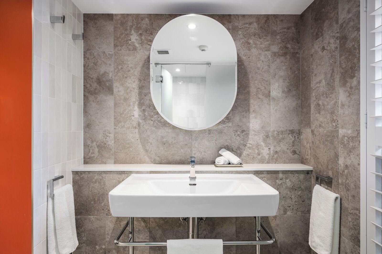 A modern bathroom with a large oval mirror, a rectangular sink, and a towel rack.