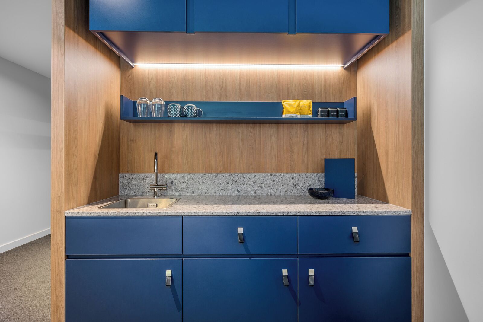 A compact kitchen with blue cabinets, a granite countertop, and a built-in shelf above the sink.