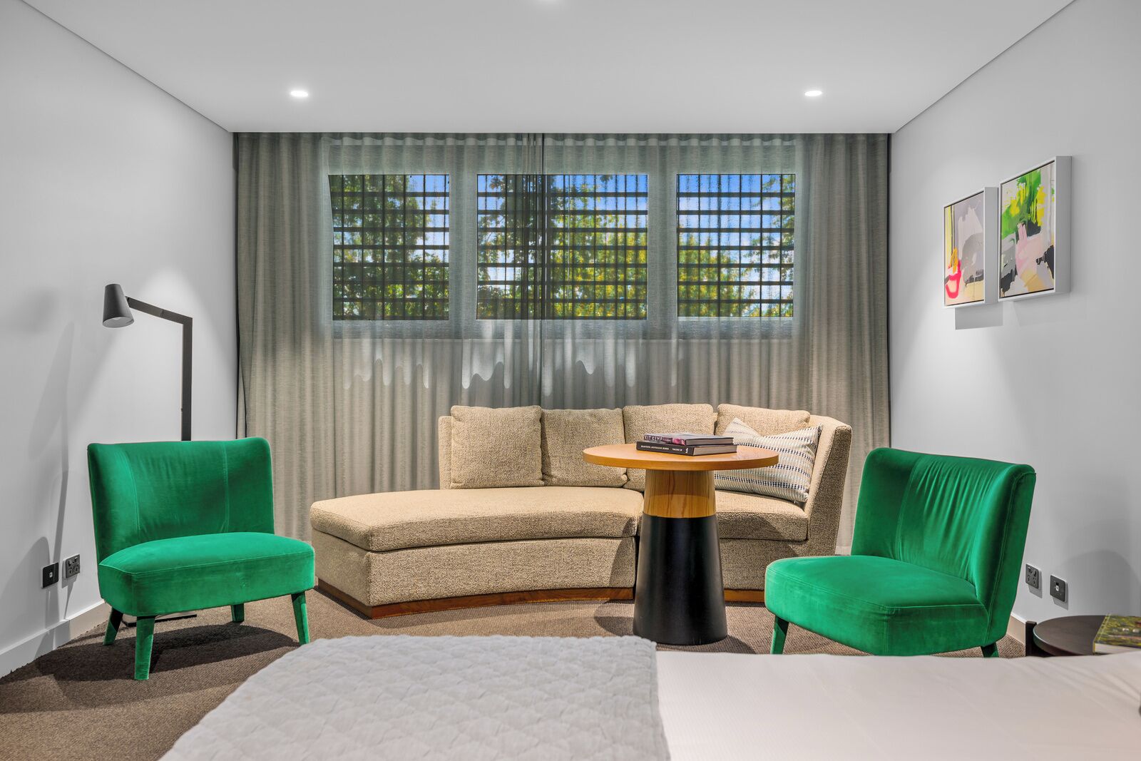 A modern living room with a beige sectional sofa, two green armchairs, a round wooden coffee table, and a floor lamp.