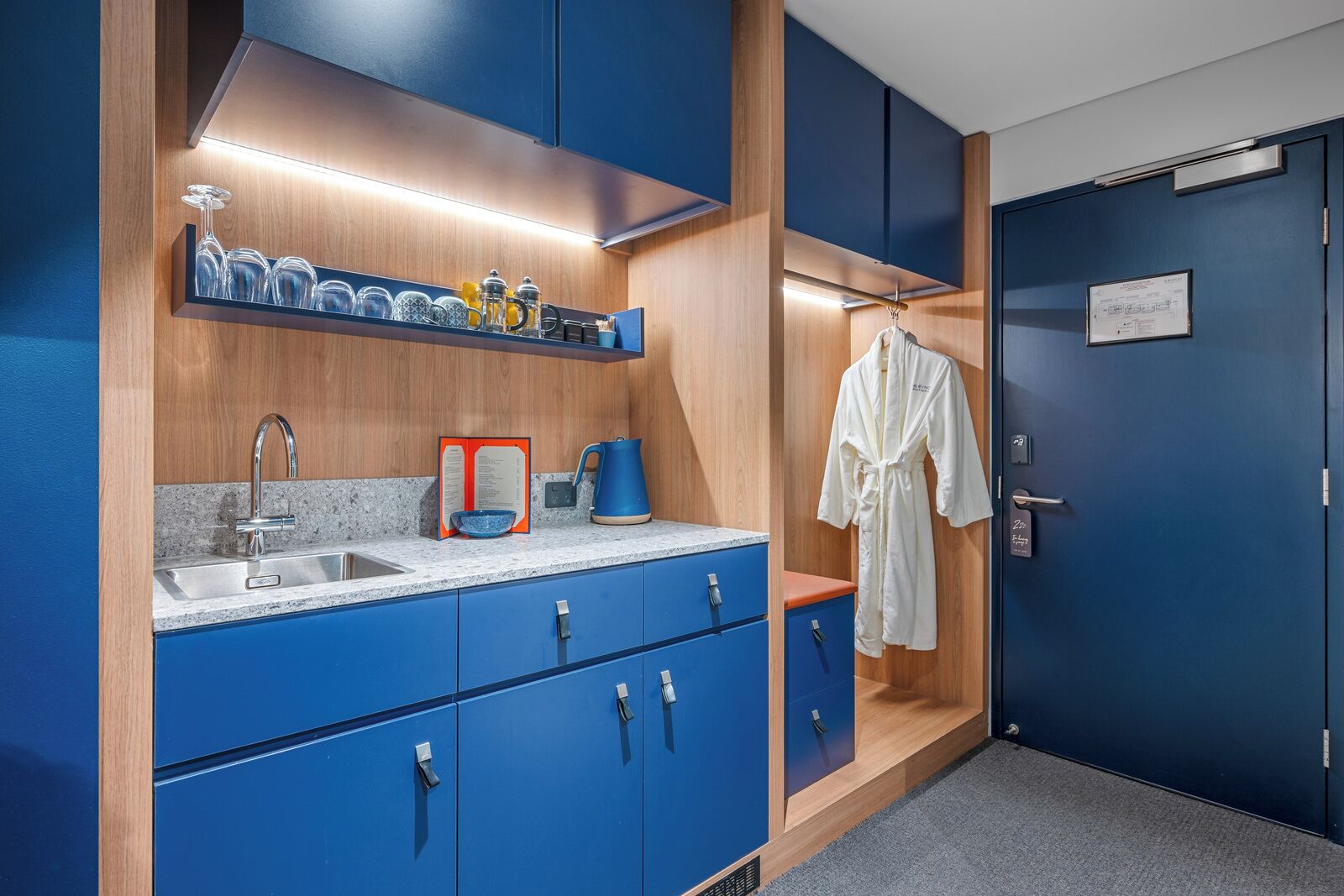 A modern bathroom with blue cabinets, a sink, and a robe hanging on the wall.