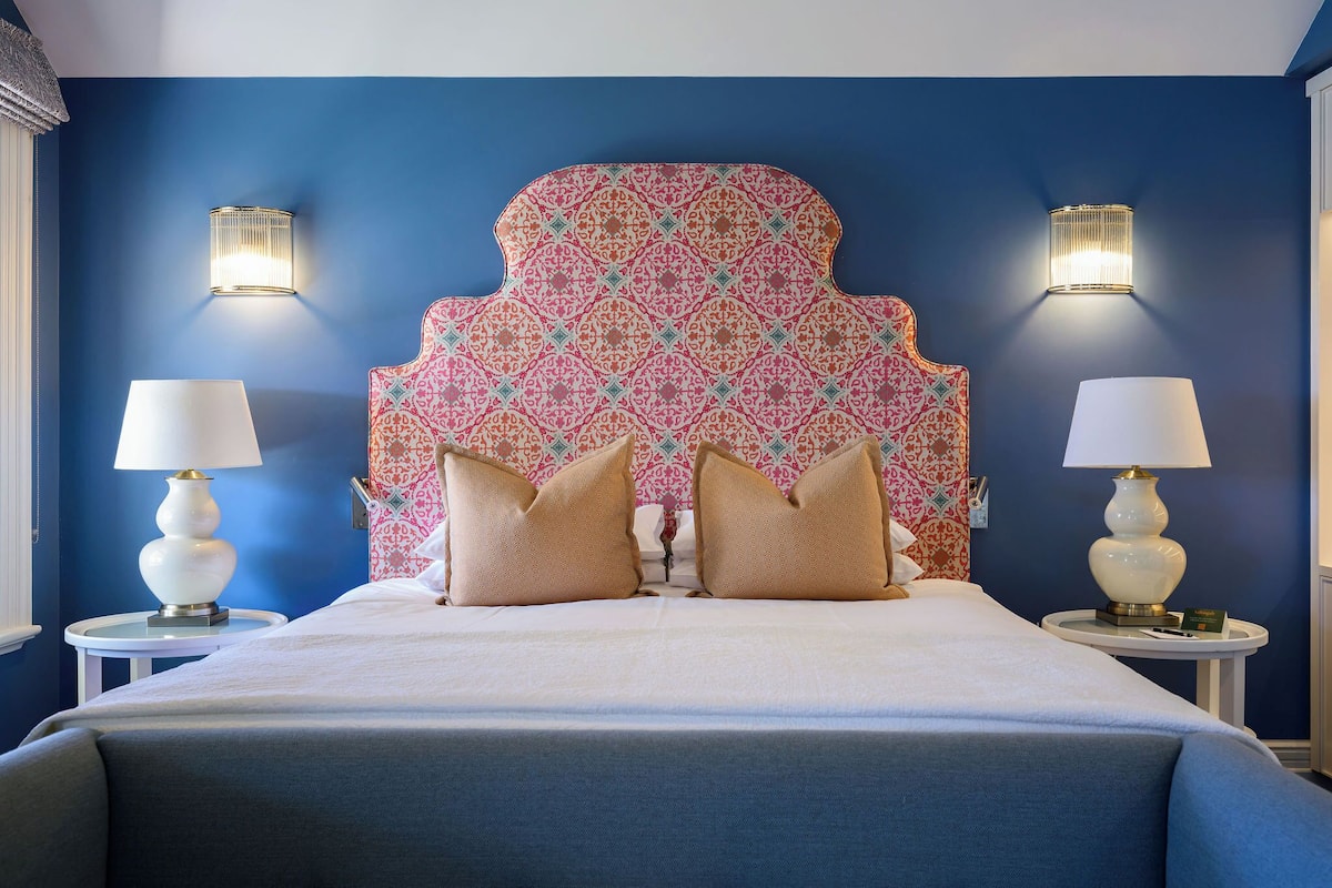 Una habitación de hotel con una cama grande, dos lámparas de noche y un cabecero estampado.