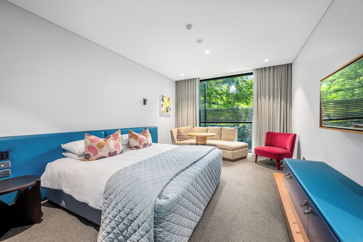 Una habitación de hotel moderna con una cama grande, un sofá, un sillón rojo y un escritorio.