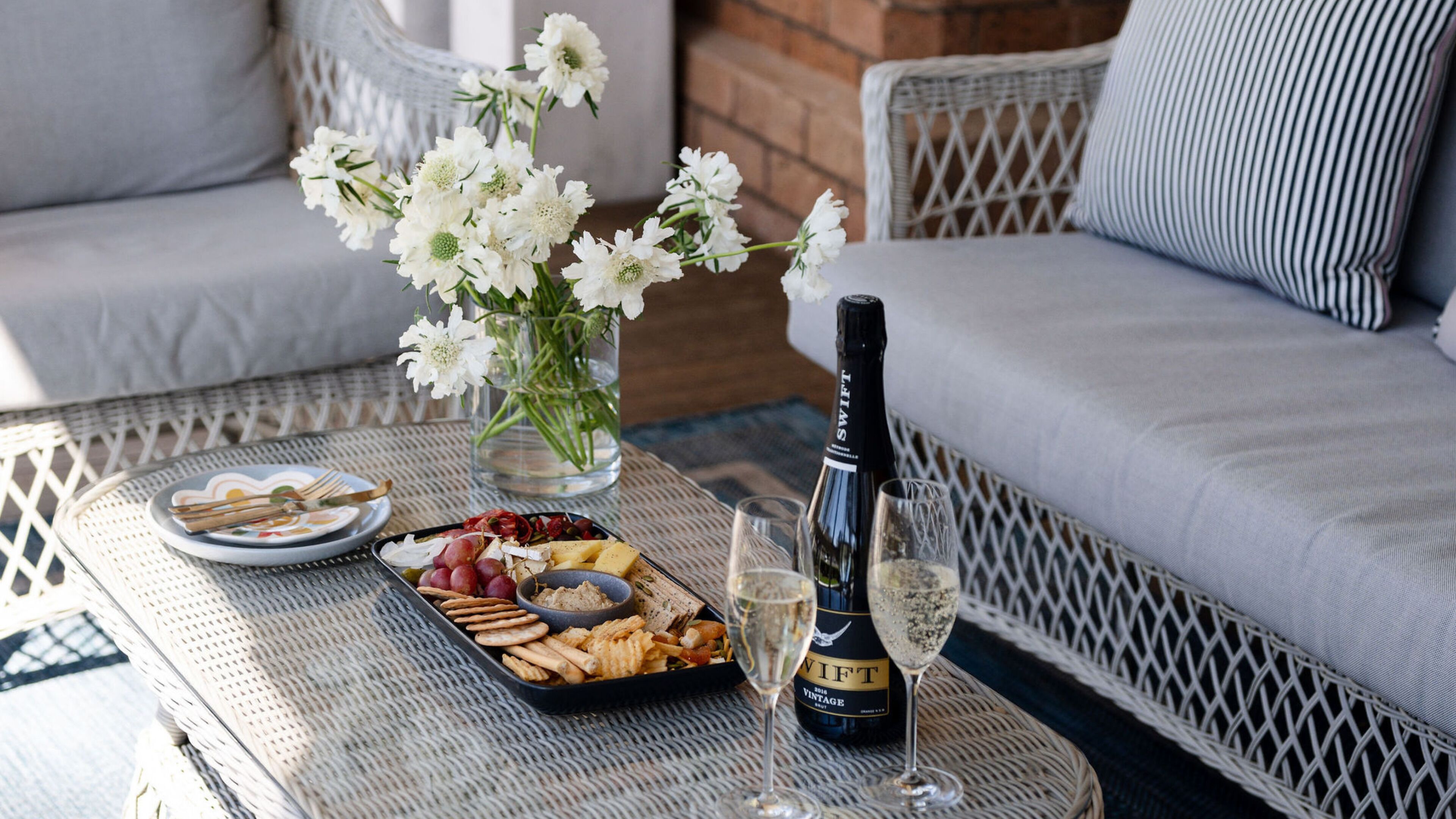 Une table en osier, avec une bouteille de champagne, un verre et une assiette de petites bouchées.