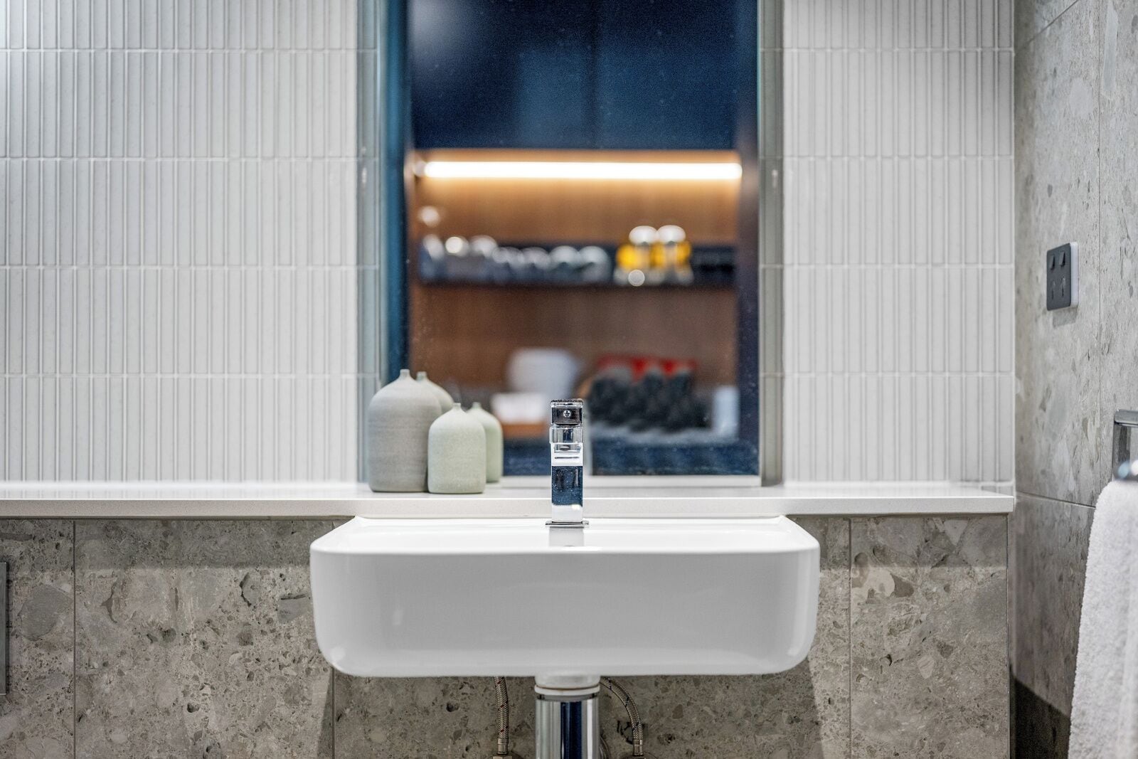 A bathroom with a white sink, a window, and a view of a kitchen area.
