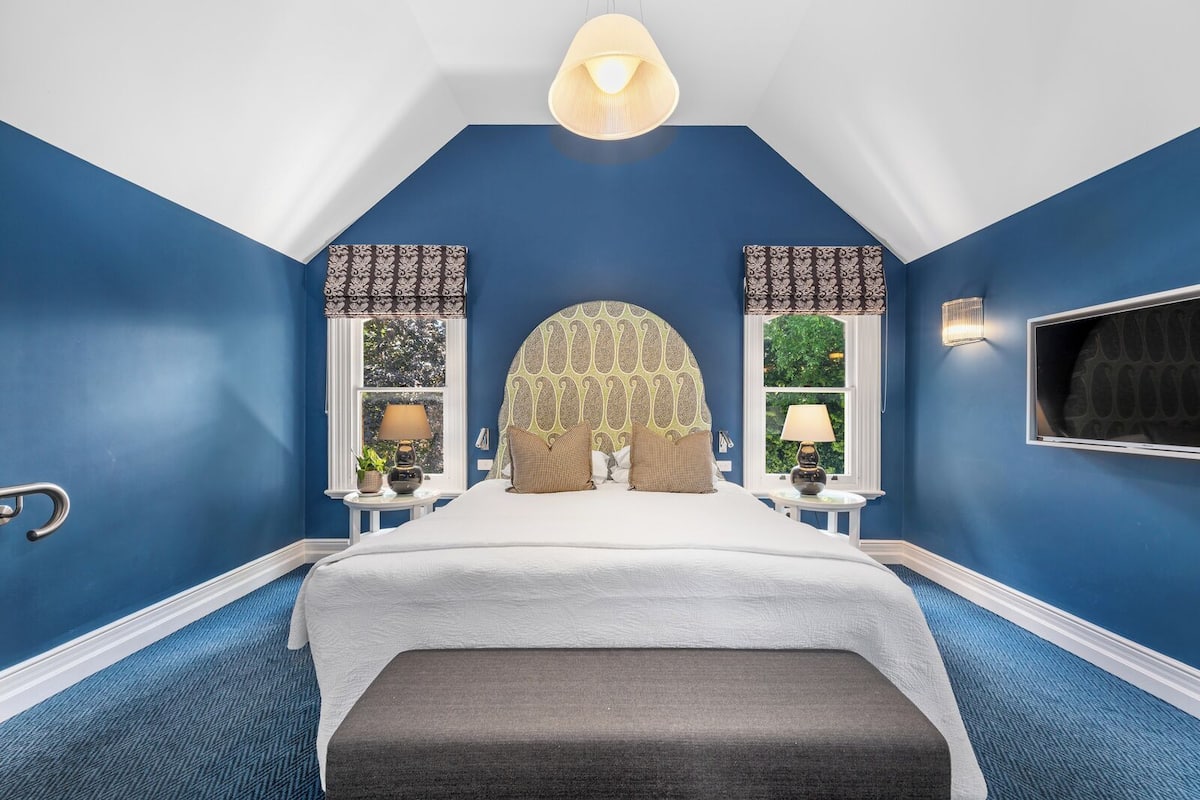 Un dormitorio con una cama grande, dos mesitas de noche con lámparas, una ventana con vistas y una lámpara de techo.