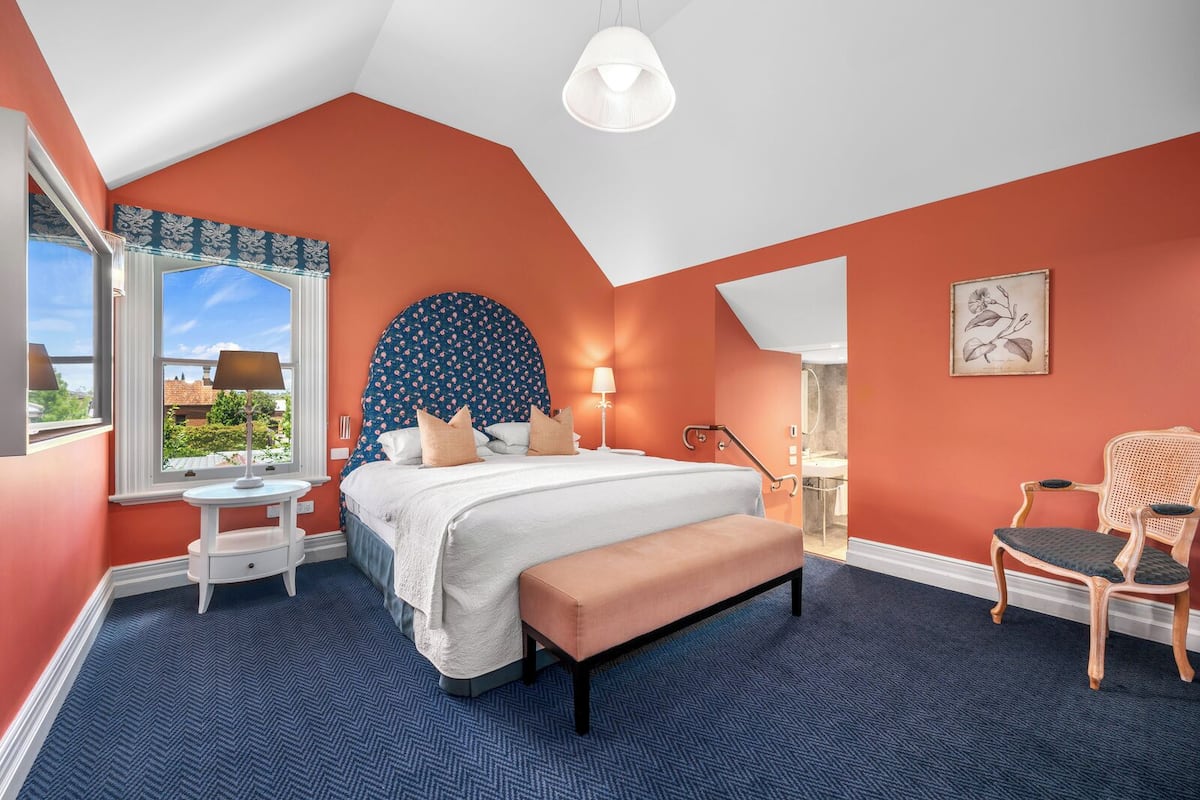 Un dormitorio con una cama grande, un escritorio, una silla y una ventana con vista a follaje.