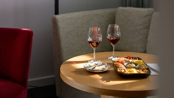 A round wooden table with a plate of snacks, two glasses of red wine, and cutlery.