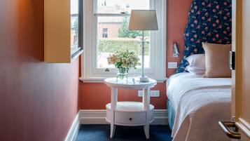 A bedroom with a bed, a bedside table with a lamp, a vase with flowers, and a window with a view of the outside.