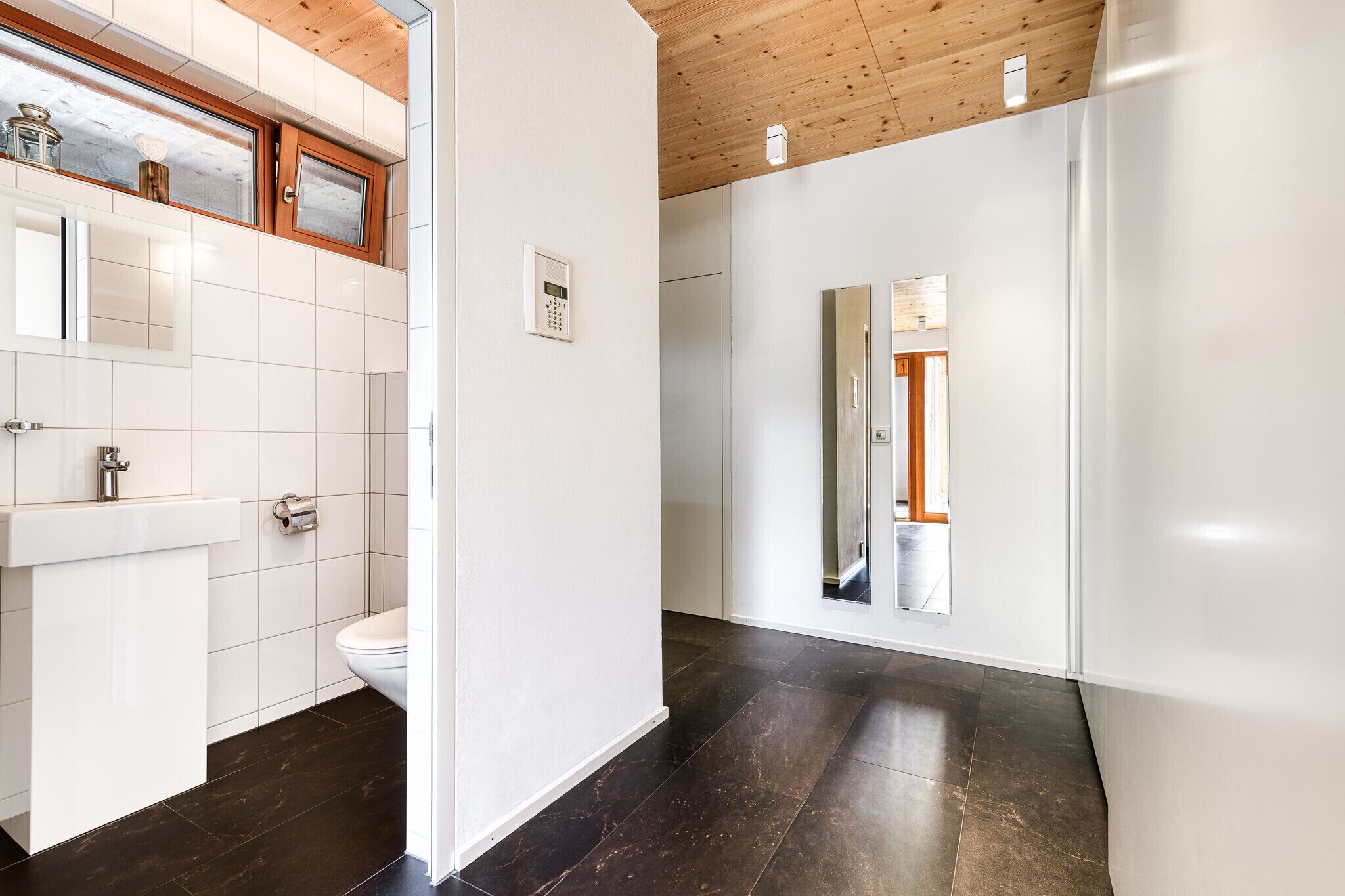 Un baño moderno con lavamanos, inodoro y suelo de baldosas oscuras.