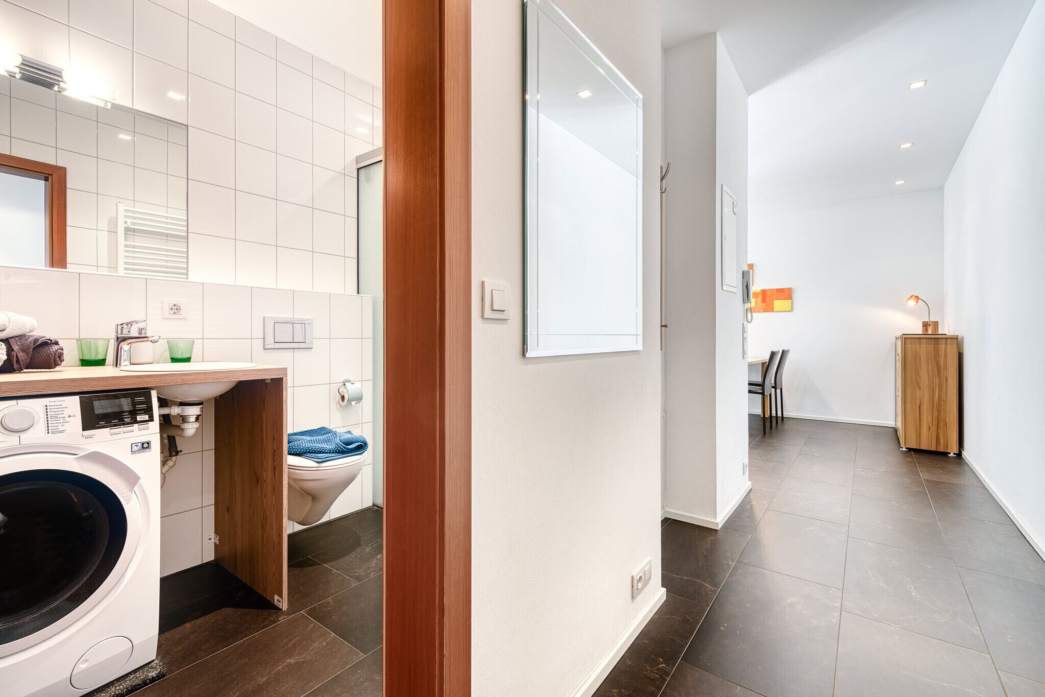 Une salle de bain moderne équipée d’un lave-linge, de toilettes et d’un miroir.