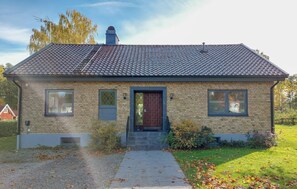 A two-story brick house with a dark roof, a front door, and two windows on the ground floor.