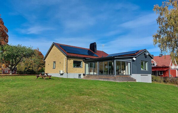 A two-story house with a red roof, solar panels, and a large glass door entrance.