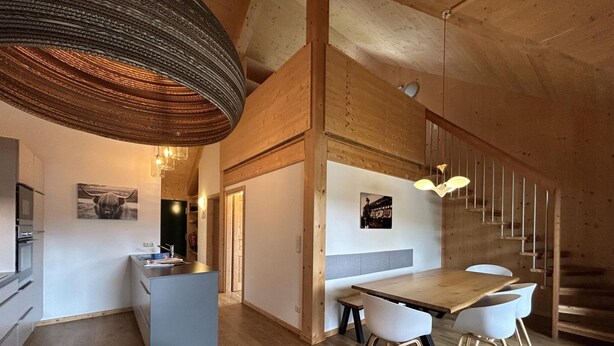 Une cuisine moderne avec des meubles en bois, un four encastré et un coin repas comprenant une table et des chaises en bois.