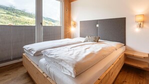 Un lit double avec une tête de lit grise, deux tables de chevet et une fenêtre avec des stores.