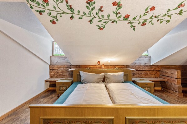 A bedroom with a wooden bed, two nightstands, a stone wall, and a floral ceiling design. - Room 'Fuchswirt 01 - Doppelzimmer' with Mountain View, Shared Garden and Wi-Fi (Kelchsau)