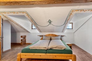 Una habitación con una cama de madera, techo inclinado con molduras decorativas y un ventanal pequeño.
