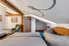 Une chambre avec un plafond de style industriel, une tête de lit en bois, un fauteuil vert et un lit avec une literie blanche.