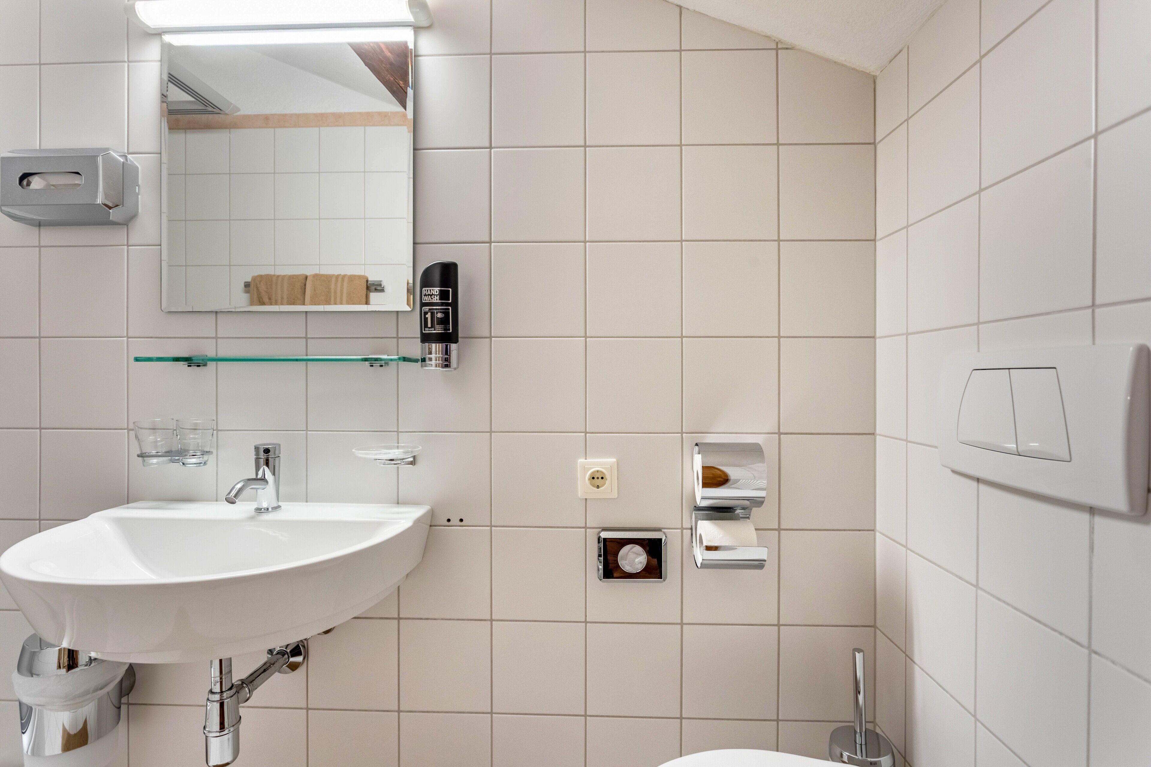 Une salle de bain avec un lavabo blanc, un miroir et des murs carrelés.