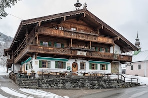A traditional wooden building with balconies, a stone staircase, and a sign indicating a restaurant.