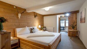 A wooden bedroom with a bed, nightstands, a lamp, a plant, and a deer skull on the wall.