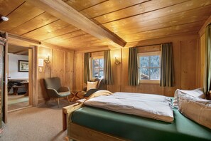 Une pièce de cabane en bois comprenant un lit, deux chaises, un bureau et une fenêtre avec des rideaux.