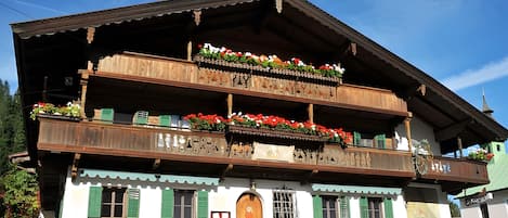 A traditional wooden building with multiple balconies adorned with flowers, a prominent wooden door, and a green roof.