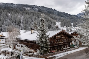 Un chalet de madera con techo cubierto de nieve, rodeado por una valla de madera y árboles nevados.