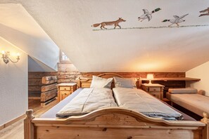 Un dormitorio acogedor en el ático con una cama de madera, dos mesitas de noche, un revistero, un banco y un mural en el techo con patos y un zorro.