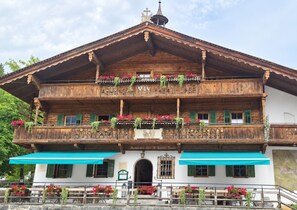 A traditional wooden building with balconies adorned with flowers, a sign indicating a restaurant, and a stone wall in the foreground. - Room 'Fuchswirt 03 - Doppelzimmer' with Mountain View, Shared Garden and Wi-Fi (Kelchsau)