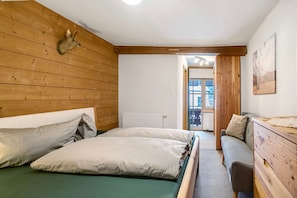 Una habitación con paredes de madera, una cama con ropa de cama verde, un aparador de madera y una cabeza de animal montada.