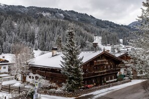 Un chalet en bois, dont le toit est recouvert de neige, entouré d’une clôture en bois et d’arbres également couverts de neige.