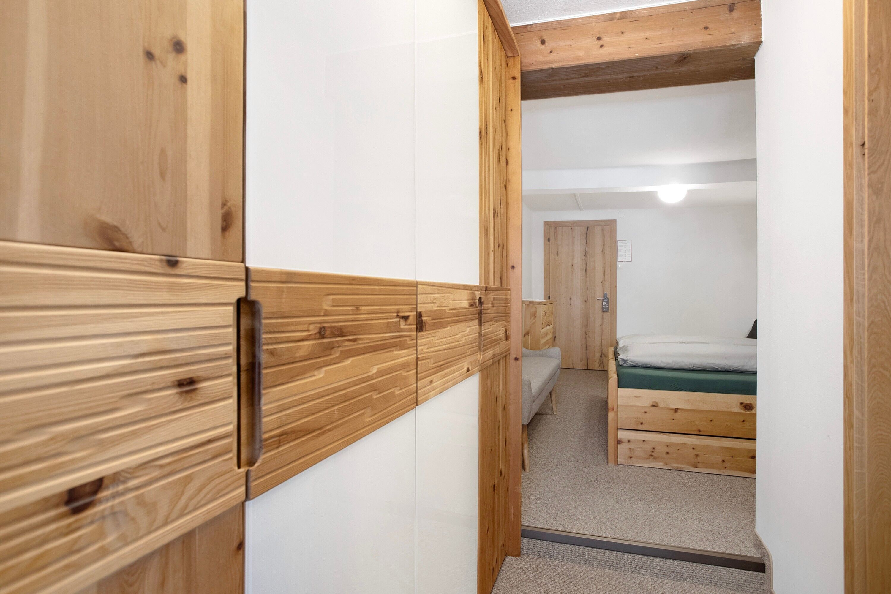 Um corredor estreito com paredes de madeira e uma cama com colchão verde no quarto.