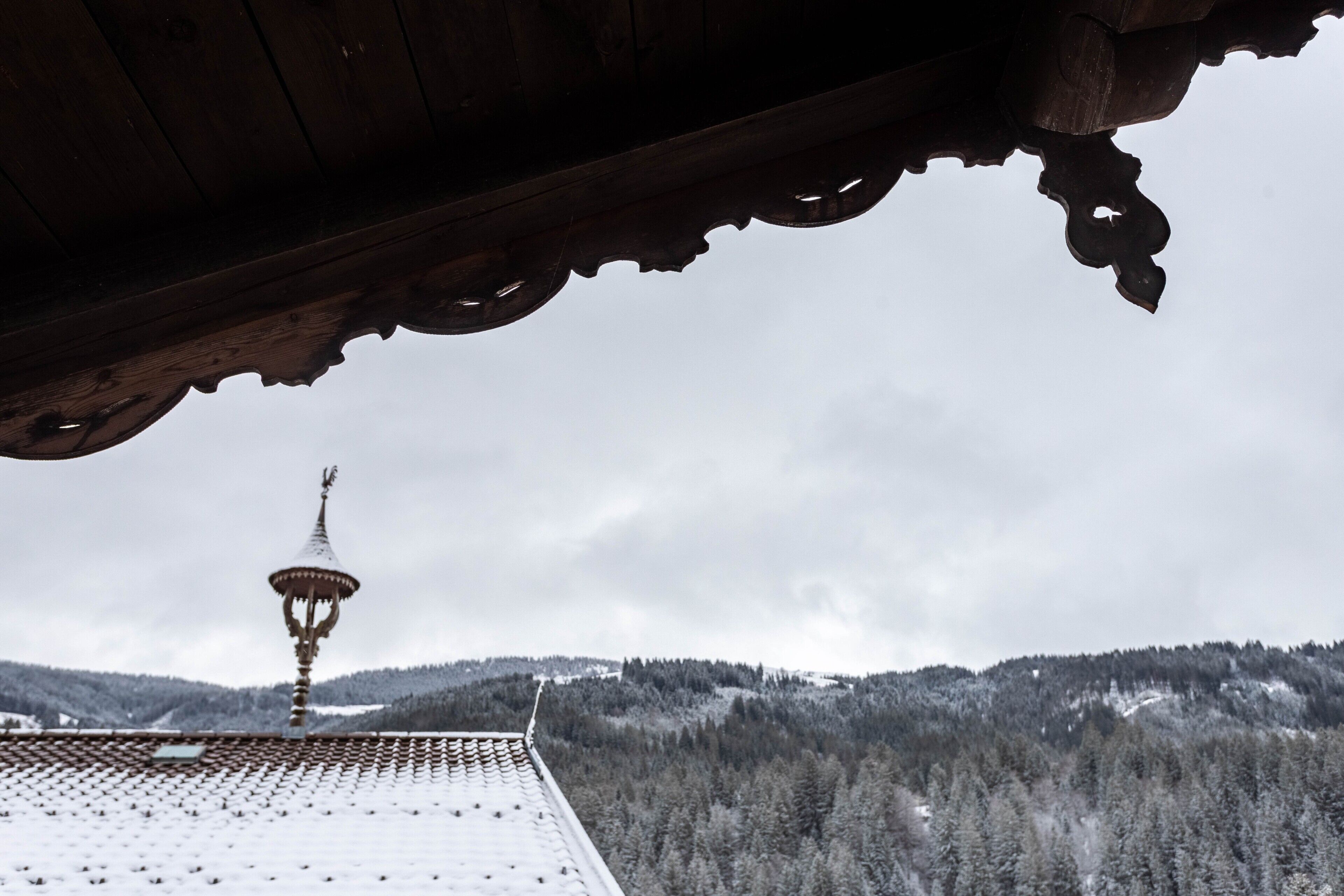 Tejado nevado con estructura de madera tradicional y una torre a lo lejos.